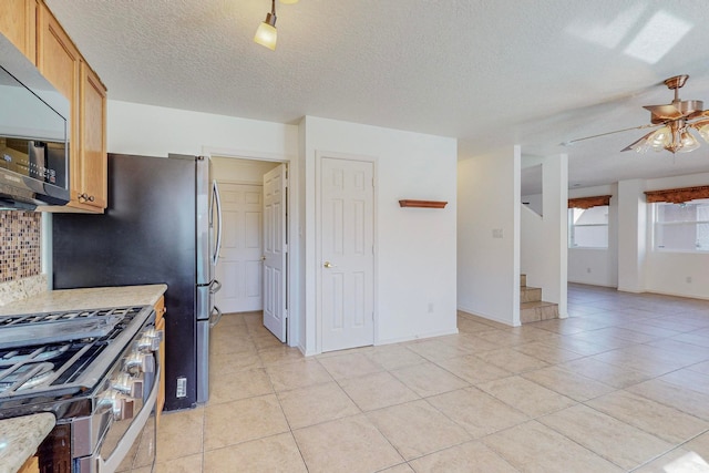 kitchen featuring backsplash, ceiling fan, appliances with stainless steel finishes, light tile floors, and a textured ceiling