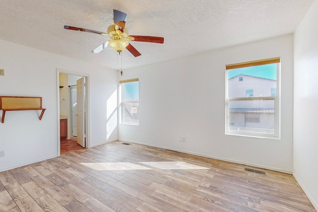 empty room with ceiling fan, a textured ceiling, light hardwood / wood-style flooring, and a healthy amount of sunlight