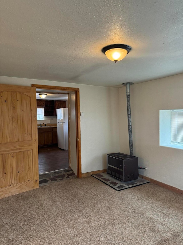 unfurnished living room with a wood stove, dark carpet, sink, and a textured ceiling