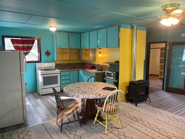 kitchen with white range with gas cooktop, refrigerator, light hardwood / wood-style floors, a wood stove, and sink