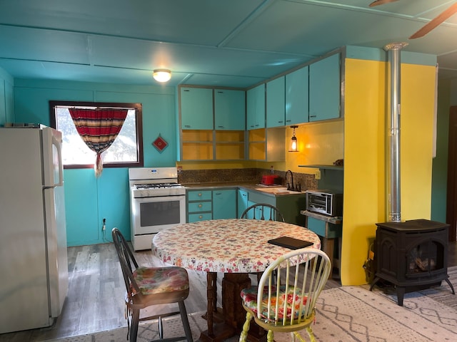 kitchen featuring a wood stove, sink, light wood-type flooring, and white appliances