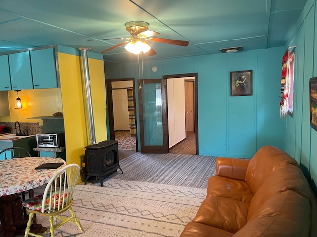 living room with carpet floors, a wood stove, and ceiling fan