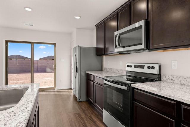 kitchen featuring appliances with stainless steel finishes, dark brown cabinets, light stone countertops, and dark hardwood / wood-style flooring