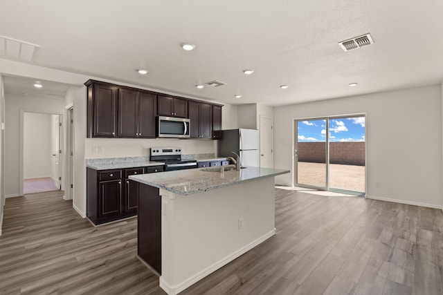 kitchen featuring an island with sink, stainless steel appliances, dark brown cabinets, dark hardwood / wood-style floors, and sink