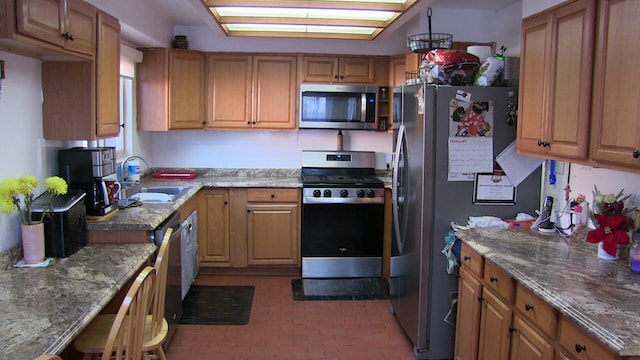 kitchen with appliances with stainless steel finishes, light stone counters, and sink