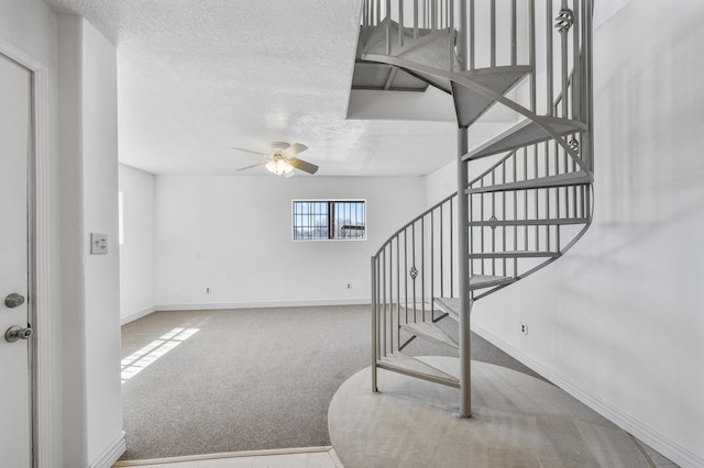 stairway with light carpet, ceiling fan, and a textured ceiling