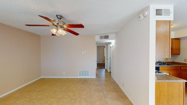 tiled empty room with a textured ceiling, ceiling fan, and sink