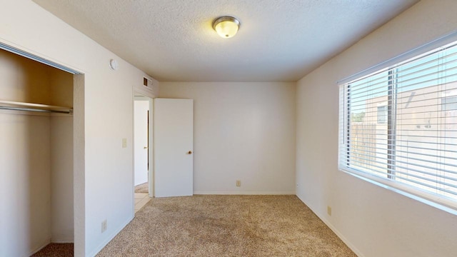 unfurnished bedroom with light colored carpet, a textured ceiling, and a closet