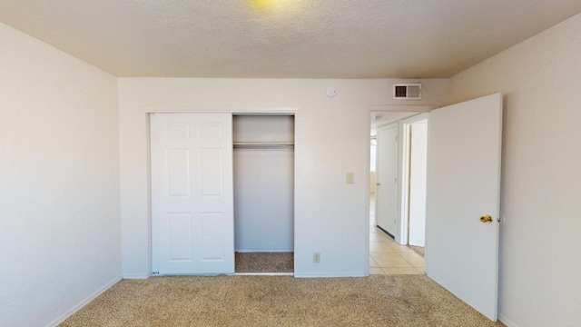 unfurnished bedroom featuring a textured ceiling, light colored carpet, and a closet