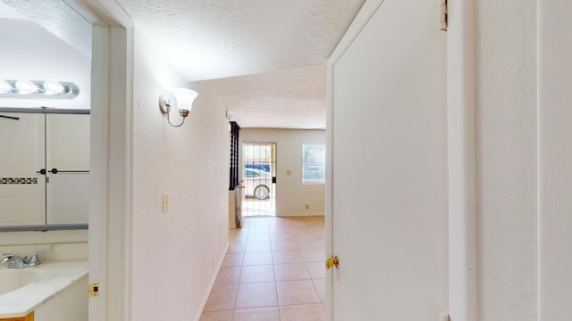 hall featuring light tile patterned floors, a textured ceiling, and vaulted ceiling