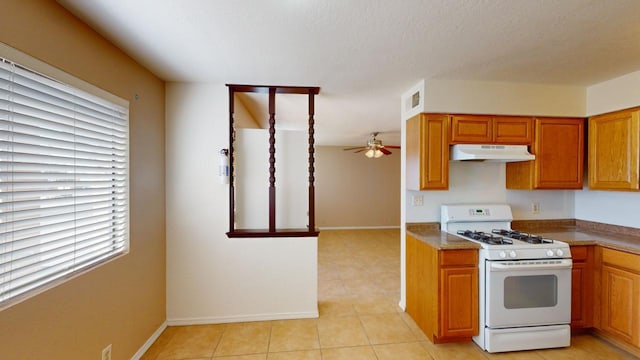 kitchen with light tile patterned floors, a textured ceiling, white gas range, and ceiling fan