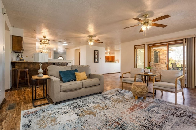 living room featuring dark hardwood / wood-style flooring, ceiling fan, and a textured ceiling