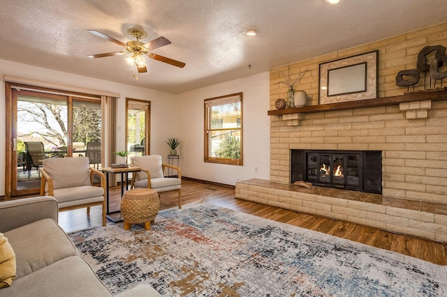 living room featuring ceiling fan, a brick fireplace, hardwood / wood-style flooring, and a textured ceiling