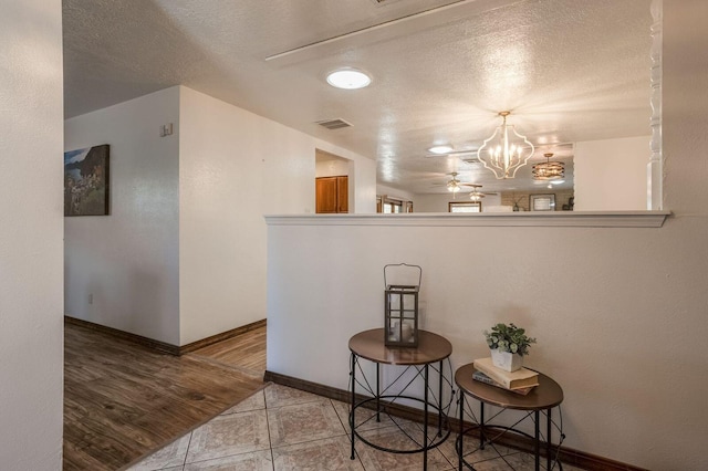 corridor featuring a textured ceiling, a notable chandelier, and light tile flooring