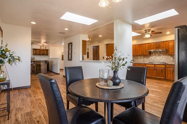 dining room featuring a skylight, ceiling fan, and light wood-type flooring