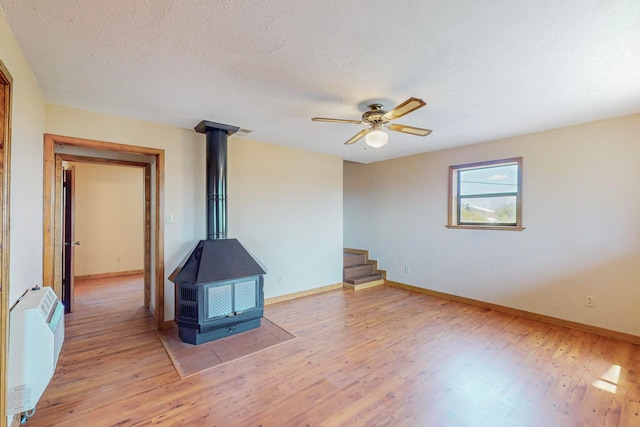 spare room featuring a textured ceiling, ceiling fan, hardwood / wood-style floors, and a wood stove