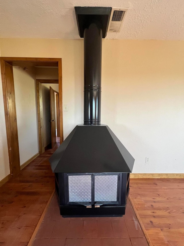 interior details with a wood stove, a textured ceiling, and hardwood / wood-style floors