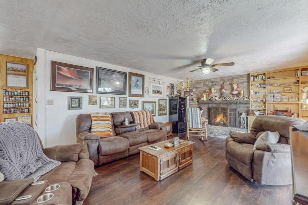 living room featuring a stone fireplace, dark wood-type flooring, ceiling fan, and a textured ceiling