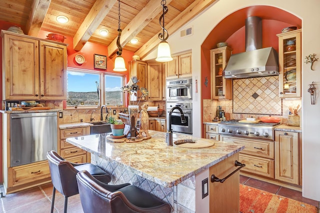 kitchen with hanging light fixtures, stainless steel appliances, light stone countertops, a center island with sink, and wall chimney exhaust hood