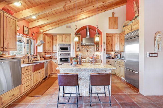 kitchen with pendant lighting, light stone countertops, stainless steel appliances, and an island with sink