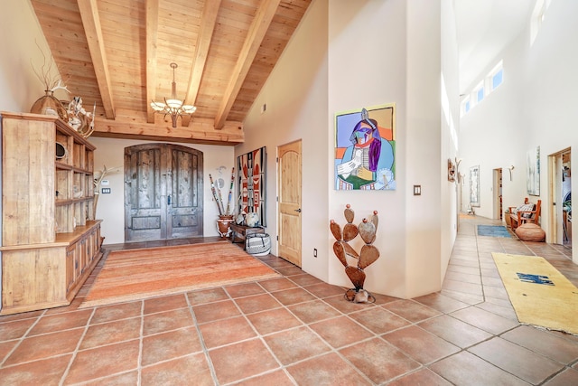 tiled entryway with high vaulted ceiling, beam ceiling, wooden ceiling, and a chandelier