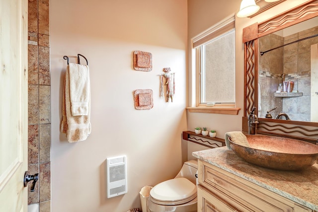 bathroom featuring heating unit, vanity, toilet, and tiled shower