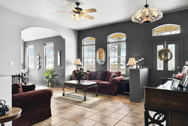 living room with a textured ceiling, light tile patterned floors, a healthy amount of sunlight, and ceiling fan with notable chandelier