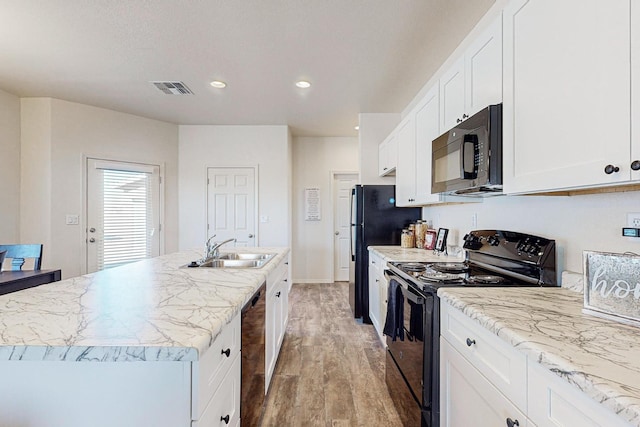 kitchen with sink, black appliances, an island with sink, white cabinets, and hardwood / wood-style floors