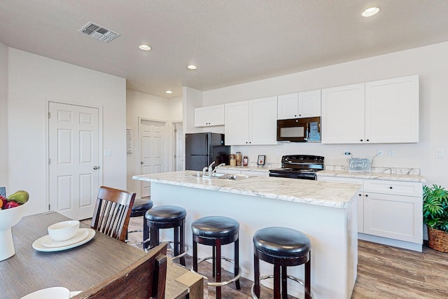 kitchen with white cabinetry, black appliances, hardwood / wood-style floors, sink, and an island with sink