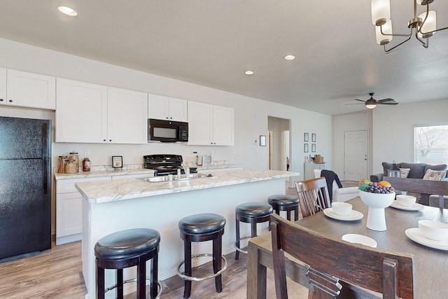 kitchen with white cabinetry, light hardwood / wood-style floors, black appliances, ceiling fan with notable chandelier, and light stone counters