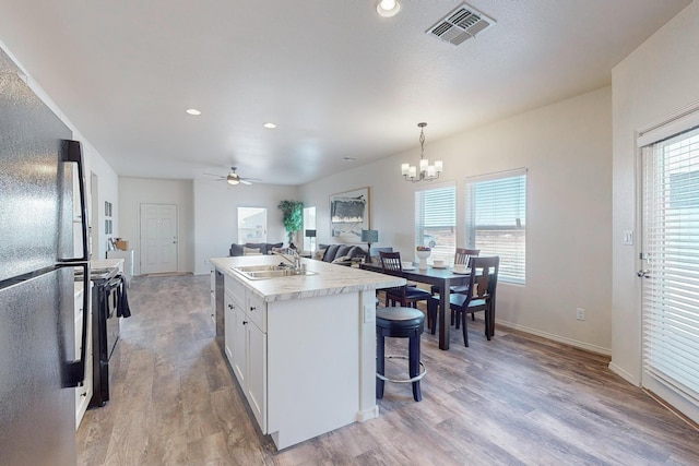 kitchen featuring ceiling fan with notable chandelier, light wood-type flooring, and an island with sink