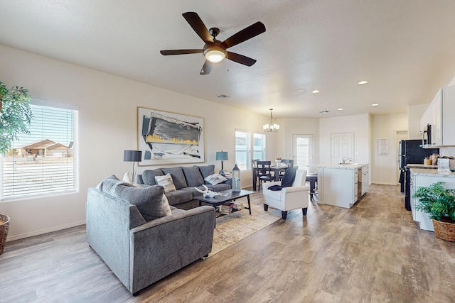 living room featuring ceiling fan with notable chandelier, light hardwood / wood-style floors, and sink