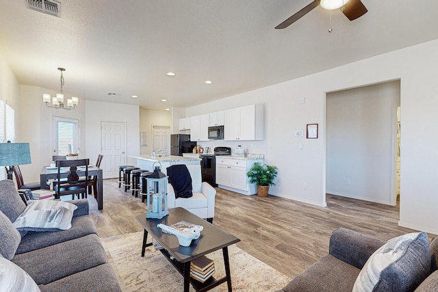 living room with ceiling fan with notable chandelier and light hardwood / wood-style flooring
