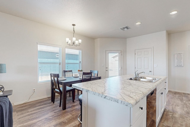 kitchen with decorative light fixtures, a center island with sink, light hardwood / wood-style floors, white cabinetry, and sink