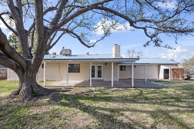 rear view of house with metal roof, a patio, french doors, stucco siding, and a chimney