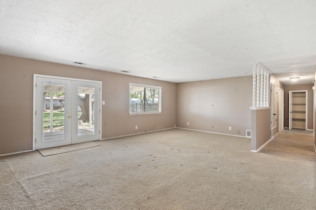 carpeted empty room featuring baseboards, visible vents, a textured ceiling, and french doors