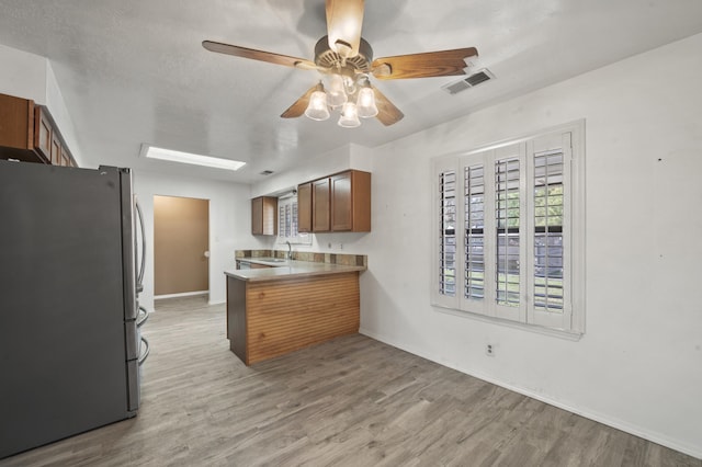 kitchen featuring visible vents, brown cabinets, freestanding refrigerator, a peninsula, and light wood-type flooring