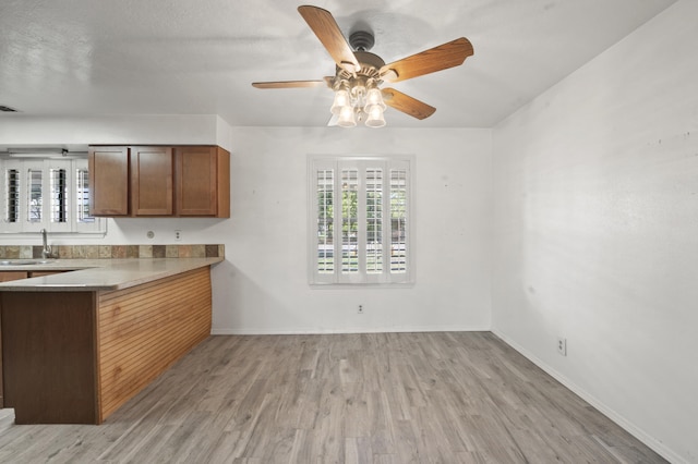 kitchen with brown cabinets, visible vents, light wood-style floors, ceiling fan, and baseboards