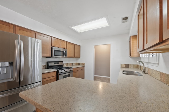 kitchen featuring stainless steel appliances, a peninsula, a sink, visible vents, and brown cabinets