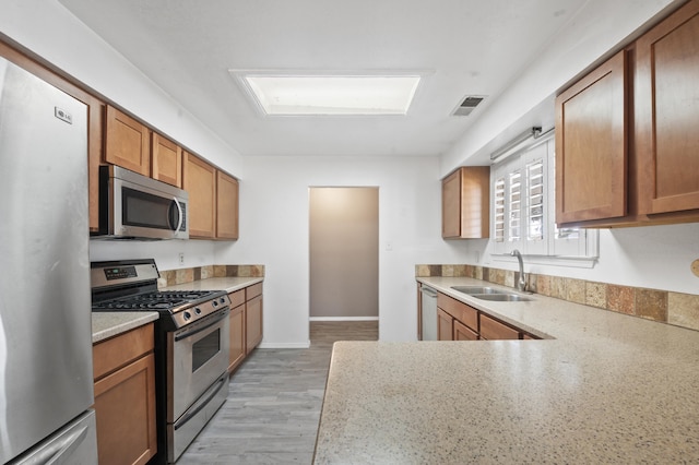 kitchen featuring stainless steel appliances, a sink, visible vents, light wood-type flooring, and brown cabinetry