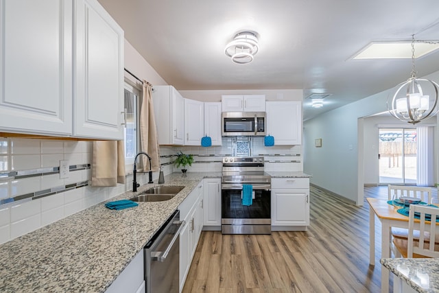 kitchen featuring sink, appliances with stainless steel finishes, white cabinets, decorative light fixtures, and light wood-type flooring