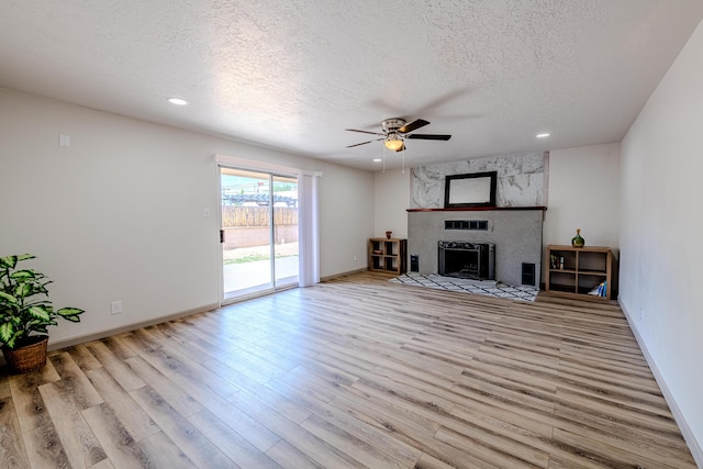 unfurnished living room with a textured ceiling, a fireplace, light hardwood / wood-style floors, and ceiling fan