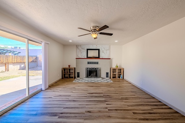 unfurnished living room with a textured ceiling, wood-type flooring, a large fireplace, and ceiling fan