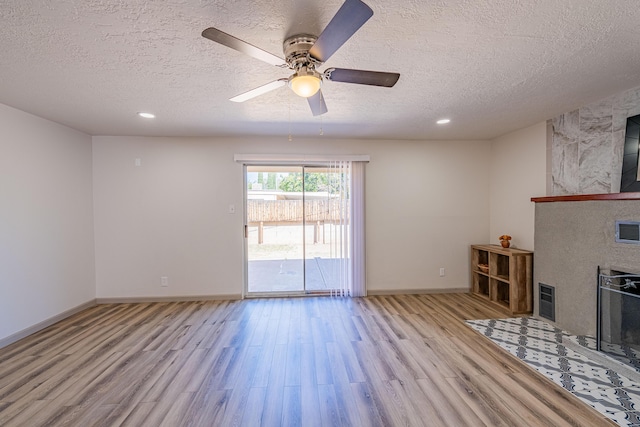 unfurnished living room featuring a tile fireplace, ceiling fan, a textured ceiling, and light hardwood / wood-style floors