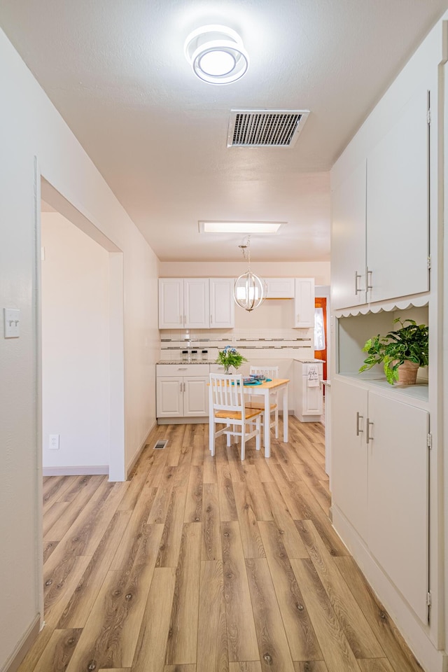 kitchen featuring a chandelier, light wood-type flooring, hanging light fixtures, and white cabinets