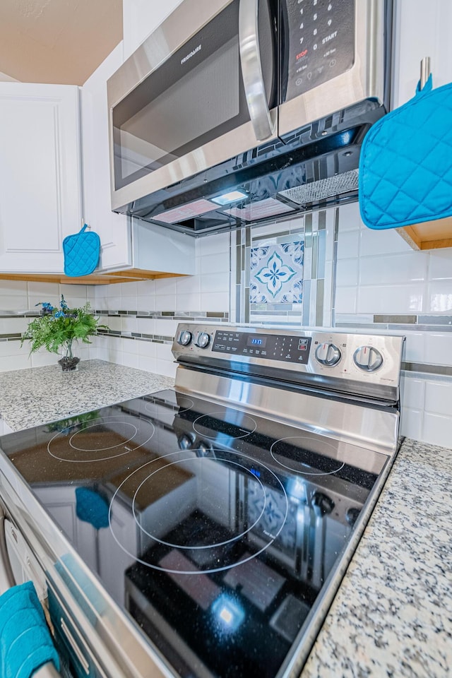 details featuring tasteful backsplash, light stone countertops, stainless steel appliances, and white cabinets