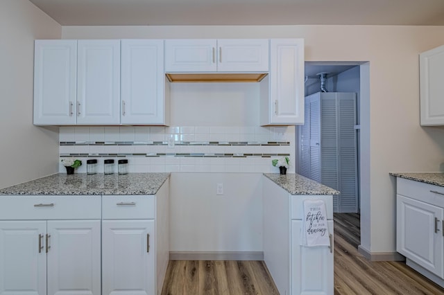 kitchen featuring white cabinetry, decorative backsplash, light stone counters, and light hardwood / wood-style floors