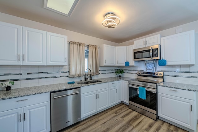 kitchen with sink, white cabinetry, light stone counters, light hardwood / wood-style flooring, and stainless steel appliances