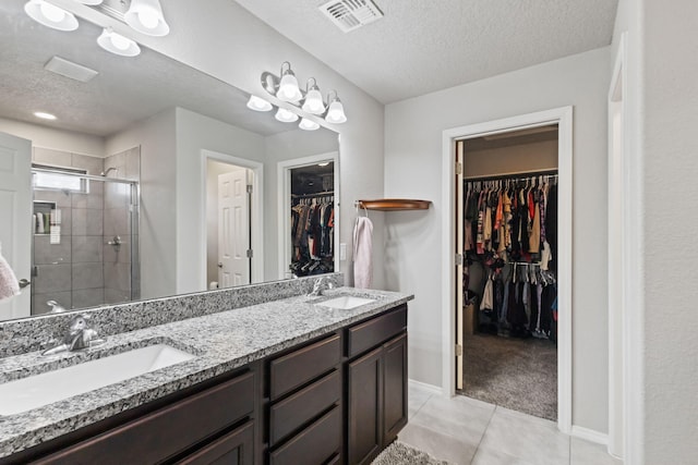 bathroom featuring tile flooring, a shower with door, dual vanity, and a textured ceiling