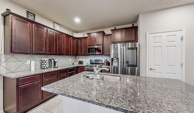 kitchen with light tile flooring, backsplash, appliances with stainless steel finishes, sink, and dark stone counters